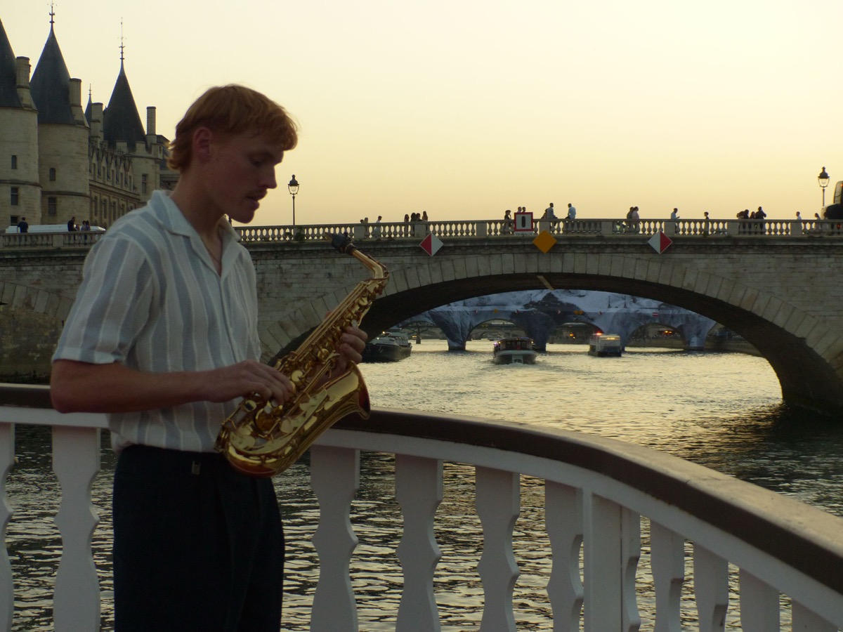 Max joue du saxophone sur une péniche, pont au Change et la Conciergerie en arrière-plan